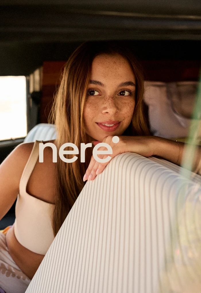 Close-up portrait of a smiling young woman with long brown hair leaning on a ridged suitcase, retouched by Iren Skaarnes