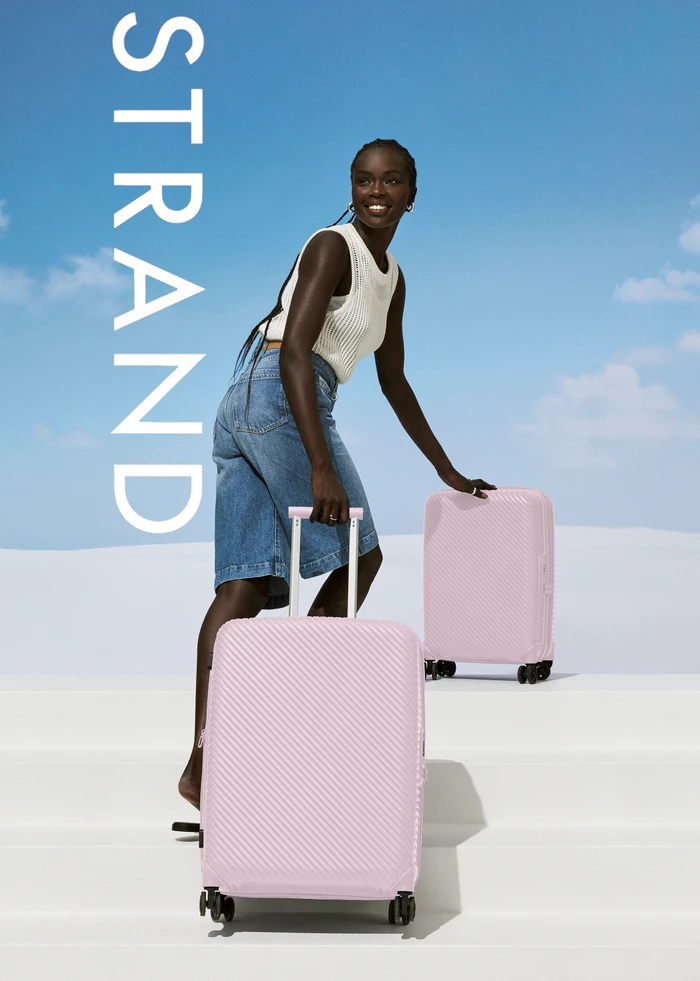 Black woman in white top and denim shorts posing with pink suitcases outdoors