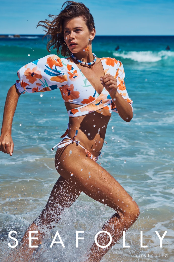 Woman in floral print bikini running through ocean surf along a sandy beach