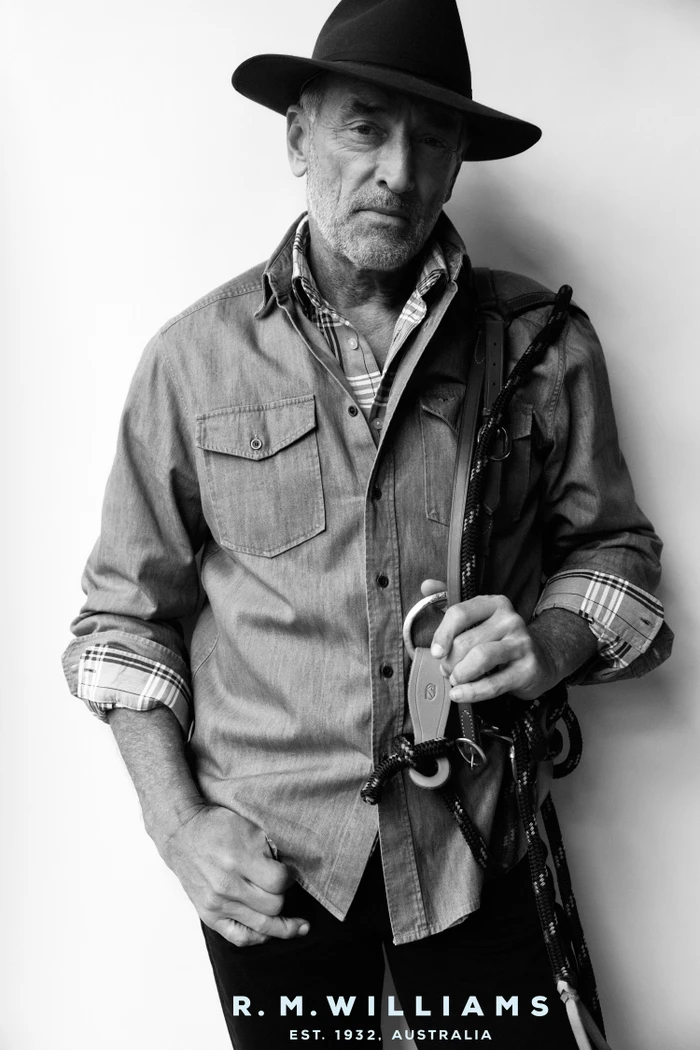 Monochrome portrait of an older man wearing a felt hat, button-down shirt, and holding rope straps.