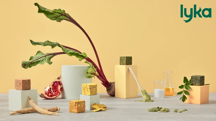 Product display featuring square food cubes on pedestals with fresh beetroot, pomegranate, and herbs on a grey wooden surface