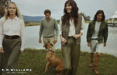 Group of four people walking outdoors near a lake with a brown dog, wearing green and neutral apparel.