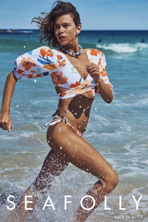 Woman in floral print bikini running through ocean surf along a sandy beach