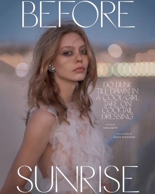 Fashion editorial portrait of a fair-skinned woman with wavy blond hair, wearing a white feathered top, against a soft bokeh background.