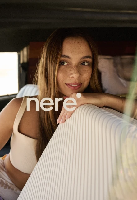 Portrait of a woman with freckles leaning on a striped surface in a vehicle, illuminated by natural light, with the brand name 'nere' visible.