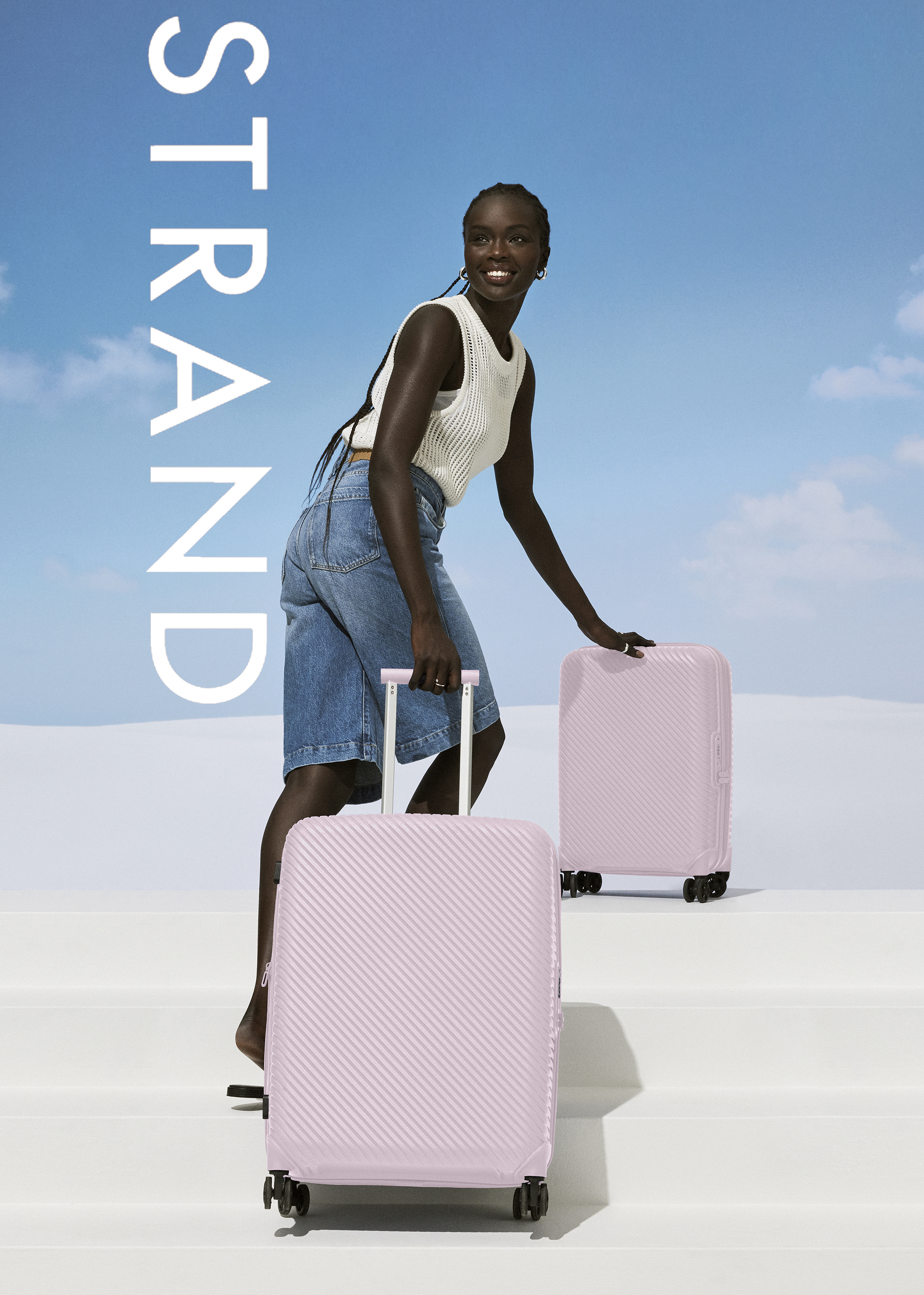 A smiling African woman in denim shorts and a top pulls two pink rolling suitcases outdoors against a sky backdrop.