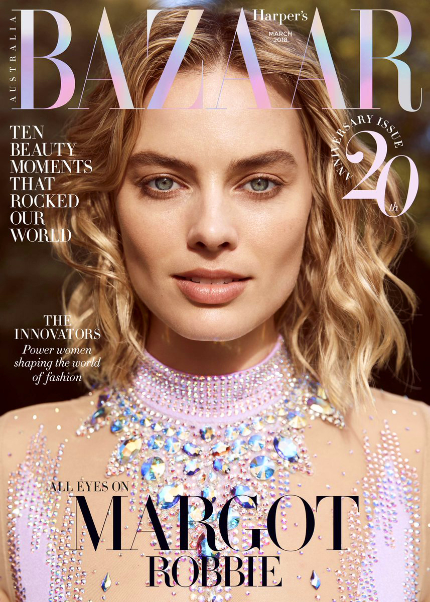 Close-up magazine cover featuring model Margot Robbie with blonde wavy hair wearing jewel-encrusted light purple dress, smiling gently.