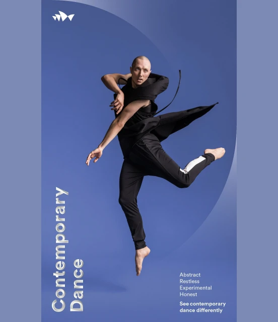 Male dancer leaping in a dance studio with a blue backdrop. He is wearing a black costume with white stripe down side of pants.