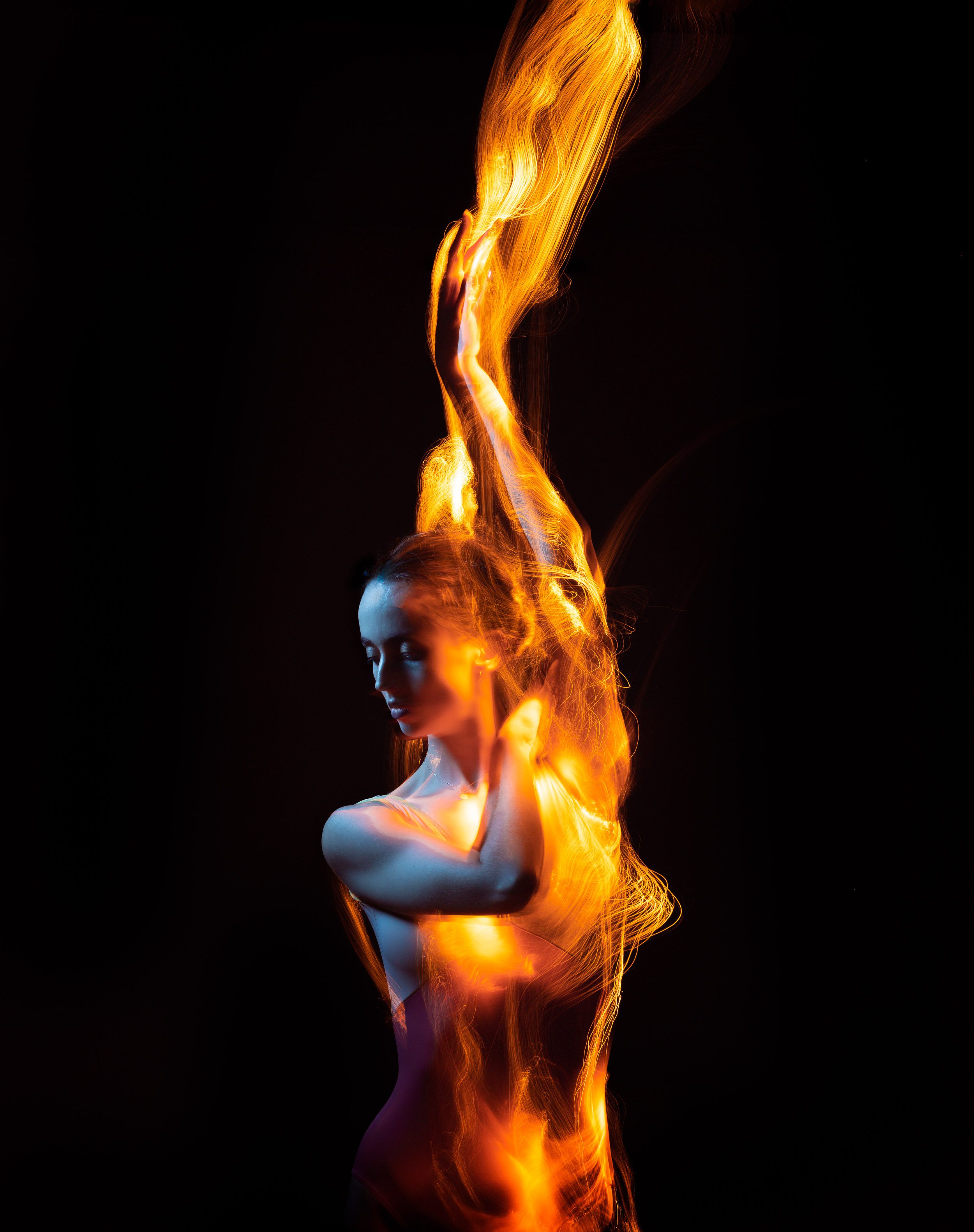 Woman portrait with dynamic light painting in oranges, reds, and yellows against a stark black background, enhancing the visual impact.