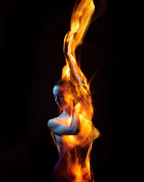 Woman portrait with dynamic light painting in oranges, reds, and yellows against a stark black background, enhancing the visual impact.