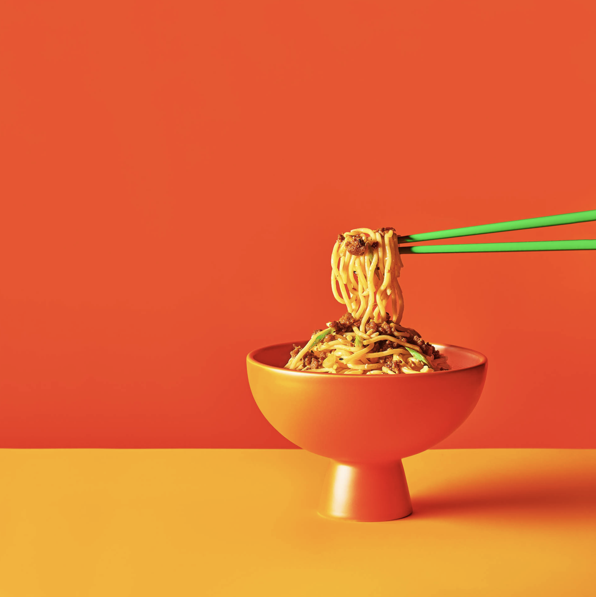 Close-up studio shot of a bowl of noodles with chopsticks against an orange and yellow backdrop, ideal for food content.