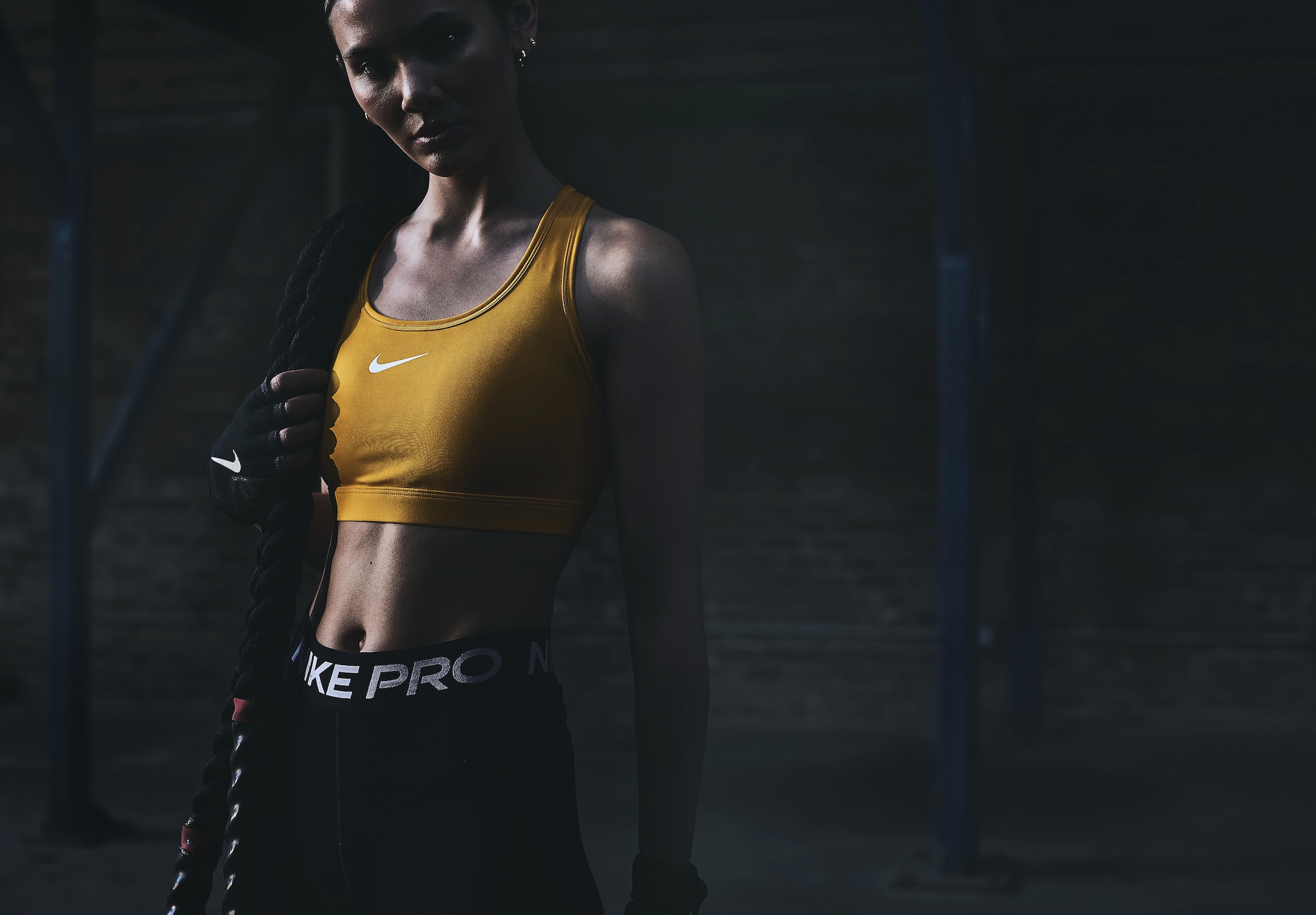 Athletic woman in workout gear poses in a fitness setting with battle ropes, showcasing strength and determination. Fitness concept.