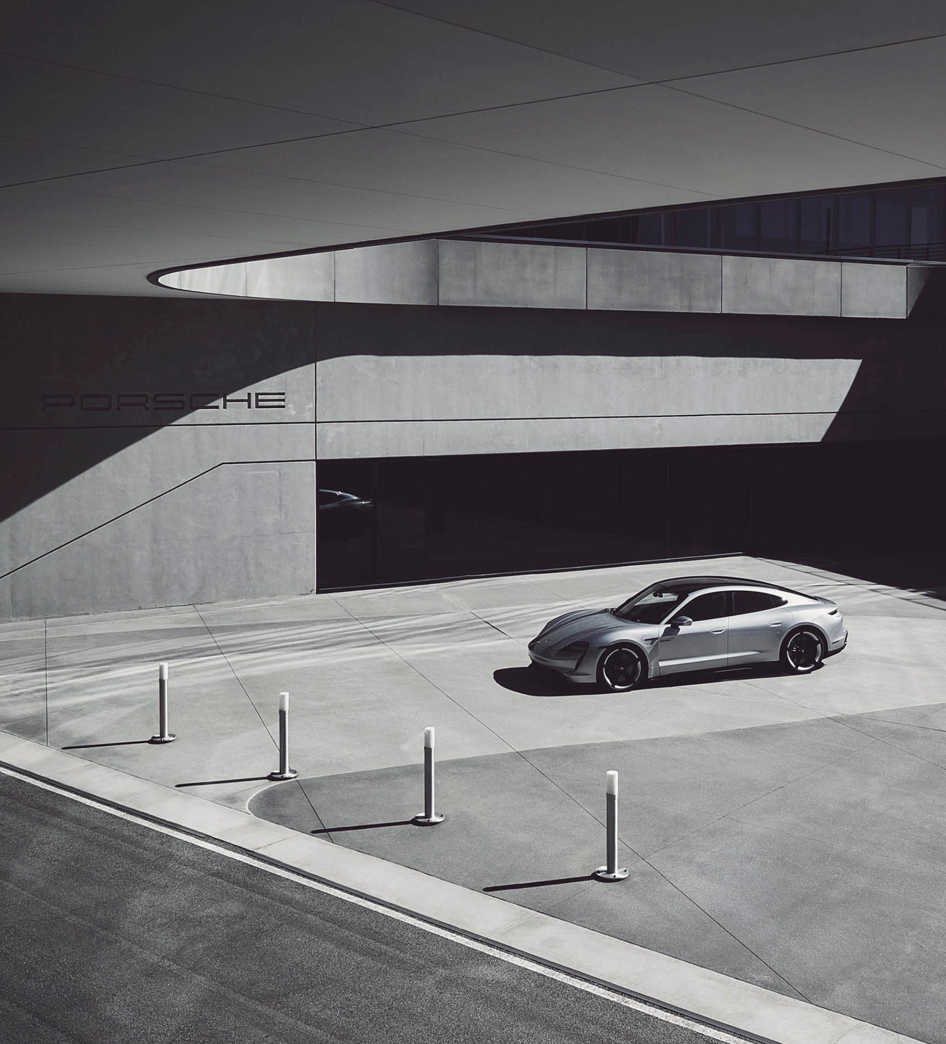 Silver Porsche parked in front of modern concrete building with minimalist architectural design and sleek lighting fixtures.