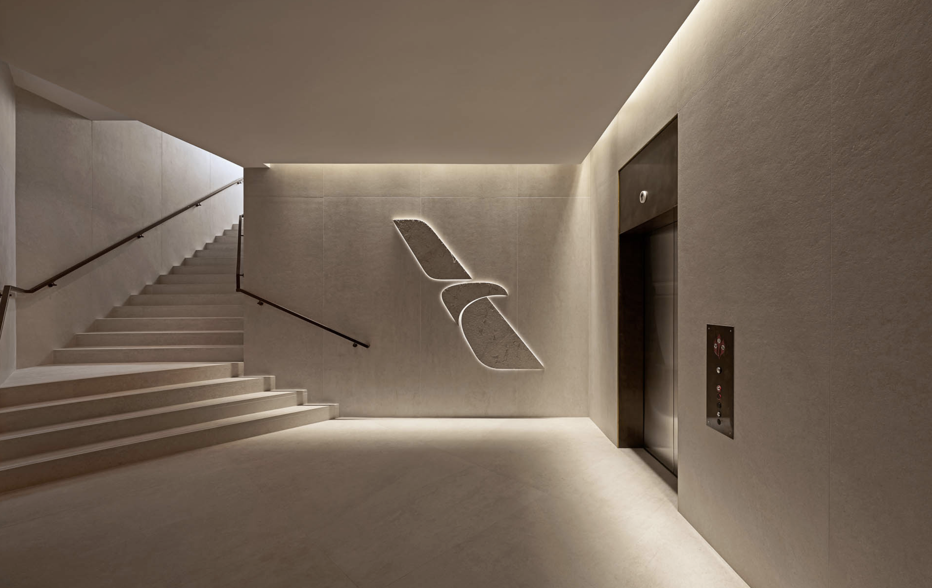 Interior of a modern building features a stairwell, an elevator, and an abstract logo of a bird on the wall, all in neutral tones.