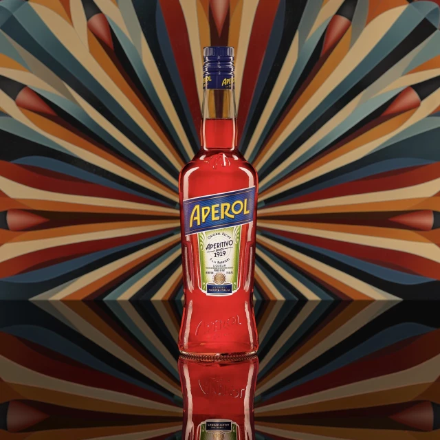 Aperol bottle on a reflective surface against a radiating patterned background, creating a vibrant and eye-catching still life.