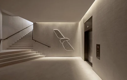 Modern minimalist interior hallway featuring a concrete staircase, elevator door, and an illuminated bird logo on the wall.