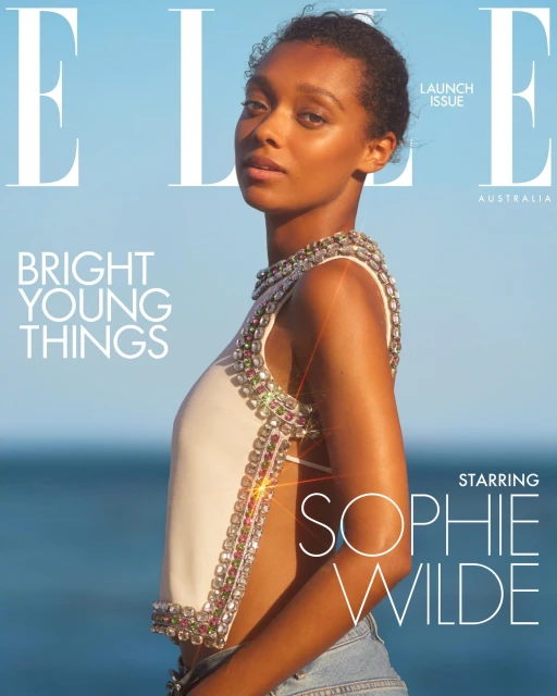 Fashion magazine cover featuring a woman with embellished top posing against an ocean and blue sky backdrop, with 'ELLE' logo.