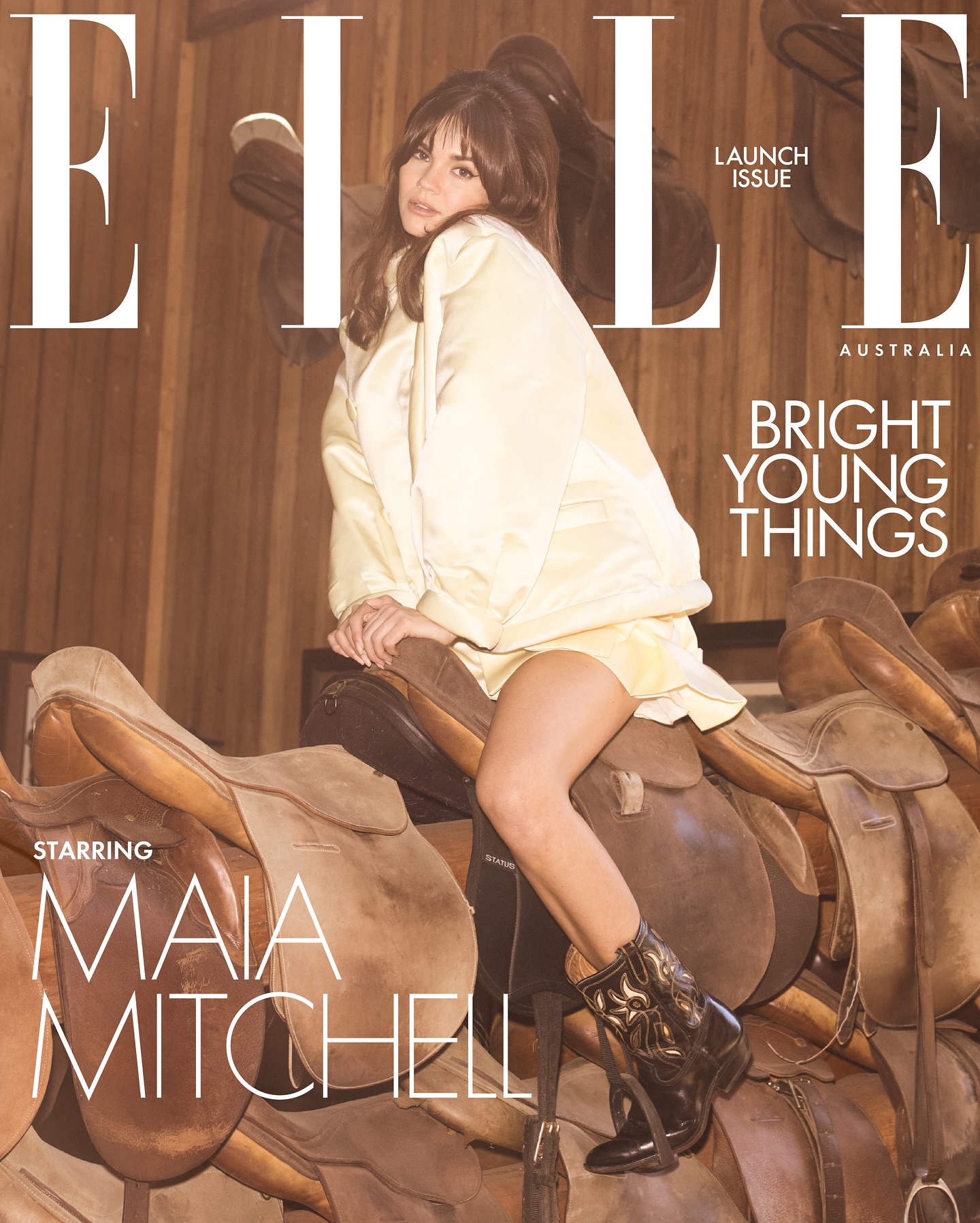 Elle Australia magazine cover featuring model Maia Mitchell seated on saddle with brown leather saddles and wood-paneled background.