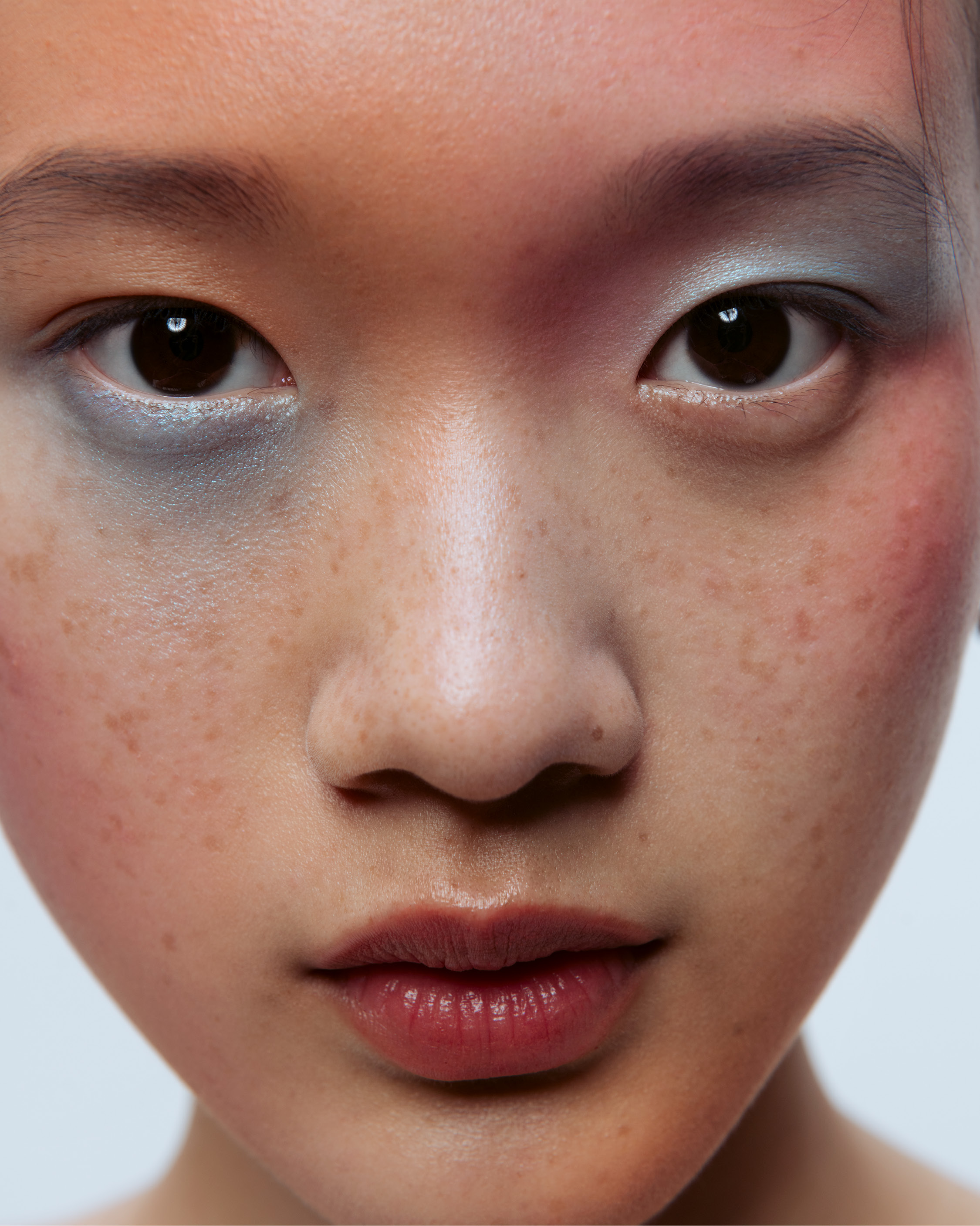 Close-up portrait of a young east asian woman featuring blue eyeshadow and visible freckles.