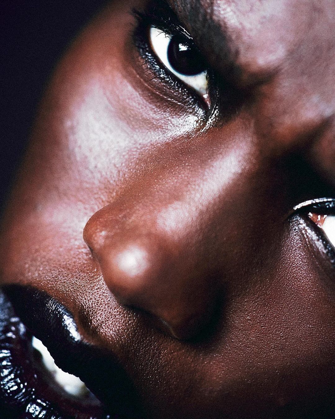 Close-up portrait of a woman with dark skin and black lipstick. The woman looks directly at the camera in this studio shot.