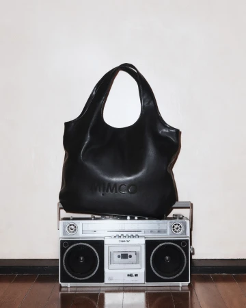 Black leather Mimco handbag sits atop a vintage boombox against a neutral wall, showcasing fashion and retro technology.