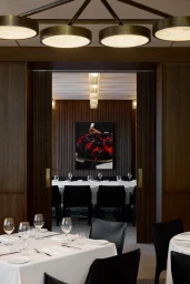 Interior view of an upscale restaurant looking through double wooden pocket doors into a private dining room with white tablecloths.