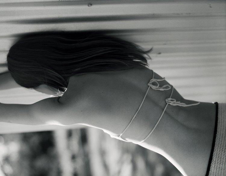 Black and white image of an adult female's bare back and shoulder in a close-up composition, with dark hair and string detail.