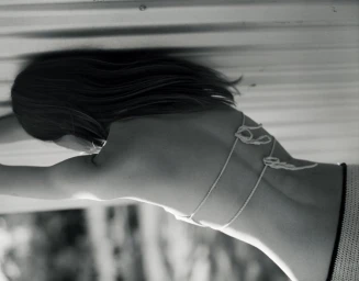 Close-up portrait of a woman wearing a white string bikini, viewed from behind against a textured background.