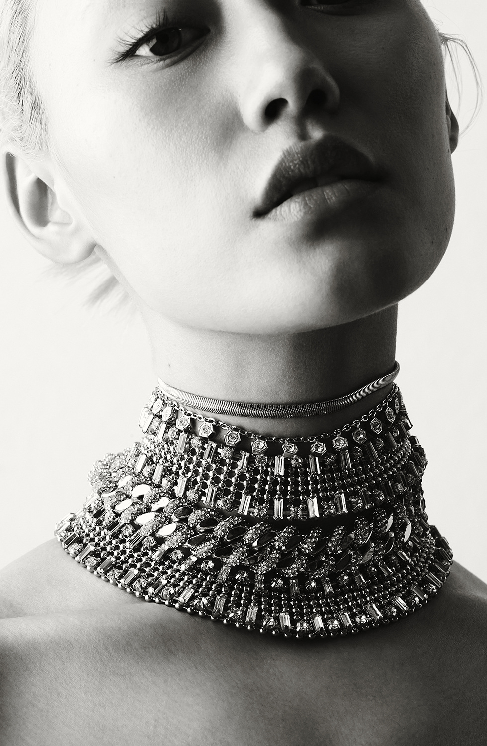 A monochrome, close-up shot featuring a model with an elaborate, jeweled choker necklace, emphasizing high-fashion beauty and intricate design.
