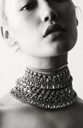 Close-up monochrome portrait of a woman wearing an elaborate rhinestone choker necklace against a white background.