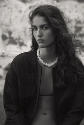 Monochrome portrait of a woman with long wavy hair wearing a quilted jacket and a textured necklace.