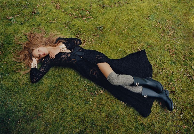 Model lying on a lush green mossy ground wearing a black lace dress and dark boots for Harper's Bazaar Australia.
