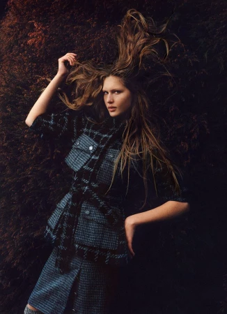 Model Angelina Kendall in a dark plaid jacket posing against dense dark foliage for Harper's Bazaar Australia.