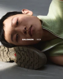 Close-up portrait of a male model resting head on a sneaker outsole for the RIER x SALOMON 2025 campaign.