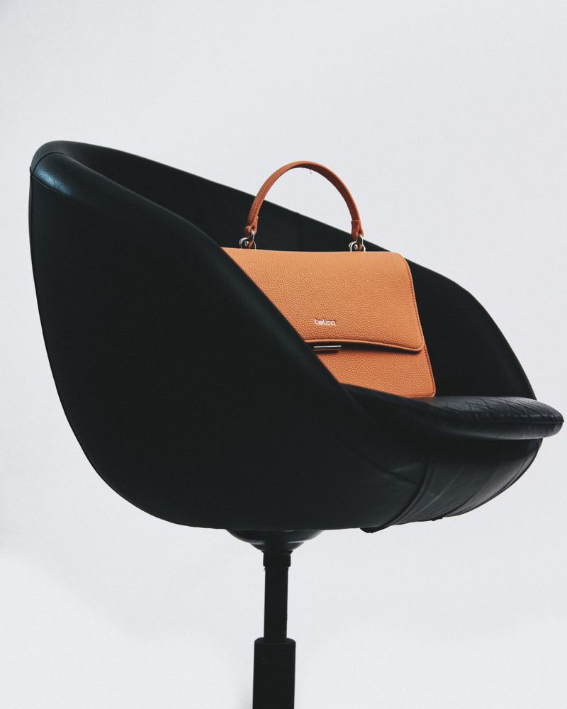 Tan leather handbag on black modern chair. The bag is sitting in a stylish, minimalist photo studio environment, fashion product.