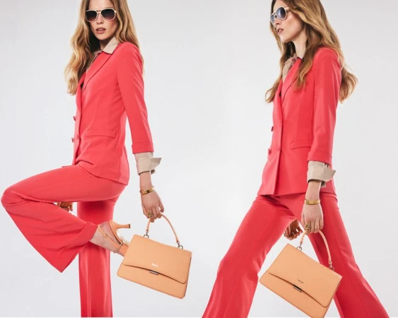 Two blonde women in red suits and sunglasses pose with handbags in a studio shot against a white backdrop, fashion-forward.