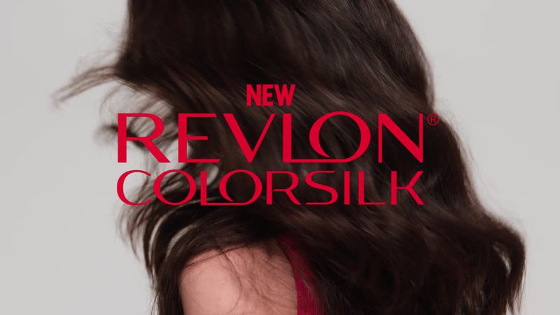 Woman with wavy brunette hair is shown in a beauty advertisement for new Revlon Colorsilk hair dye against a white background.