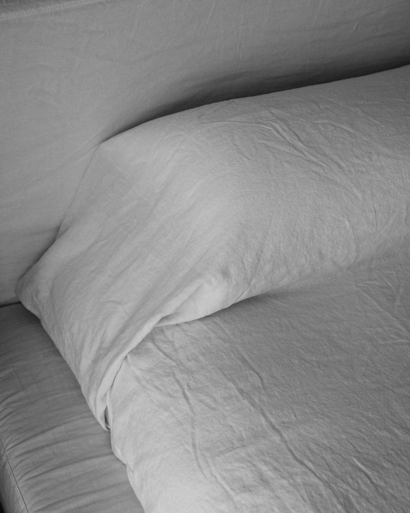 Monochrome photograph of a wrinkled white pillow and rumpled white bedding on a bed in a bedroom interior.