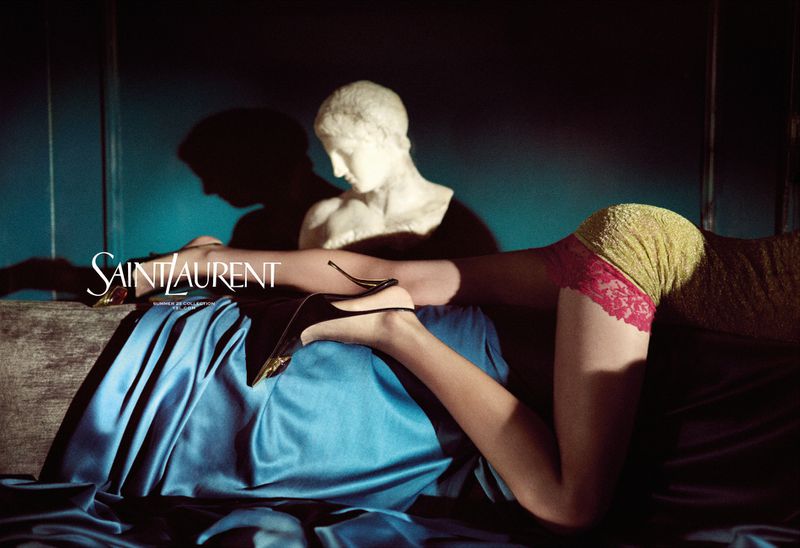 Fashion-forward advertising image featuring a woman's legs and high heels, alongside a classic marble bust and the Saint Laurent logo.