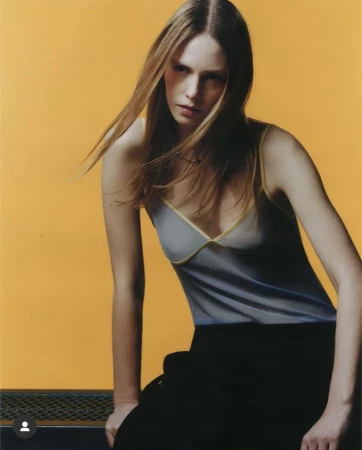 Model with long brown hair wearing a grey top against a bright yellow background for Highsnobiety.