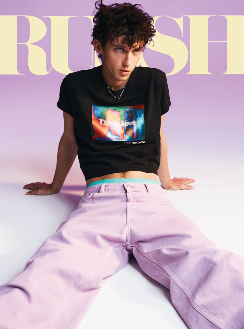 Young adult male poses in lilac pants and a black t-shirt against a faded lilac background for a studio portrait. Fashion, lifestyle.