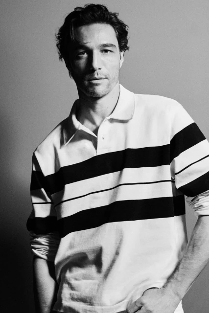 Monochrome portrait of an adult male wearing a striped polo shirt, posing indoors with a neutral facial expression.