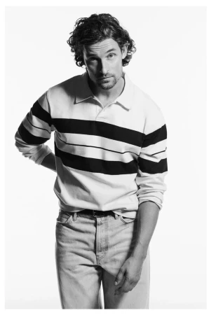 A male model wearing a striped polo shirt and jeans against a white seamless background for Zara Man 90s archive campaign.