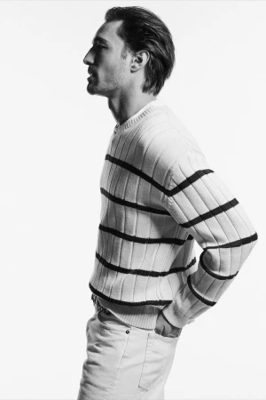 Profile view of a male model wearing a striped knit sweater against a seamless white studio background.