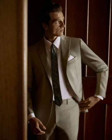 Man in a suit standing in doorway with dark wood paneling, wearing a tie and white shirt, looking away from the camera.