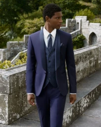 Model in navy blue tuxedo with matching vest standing on a stone terrace at Eastnor Castle for Corneliani Code 2025.