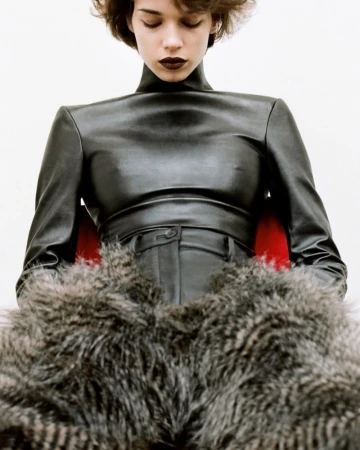 Model with dark lipstick wearing black leather top and trousers against a white backdrop.