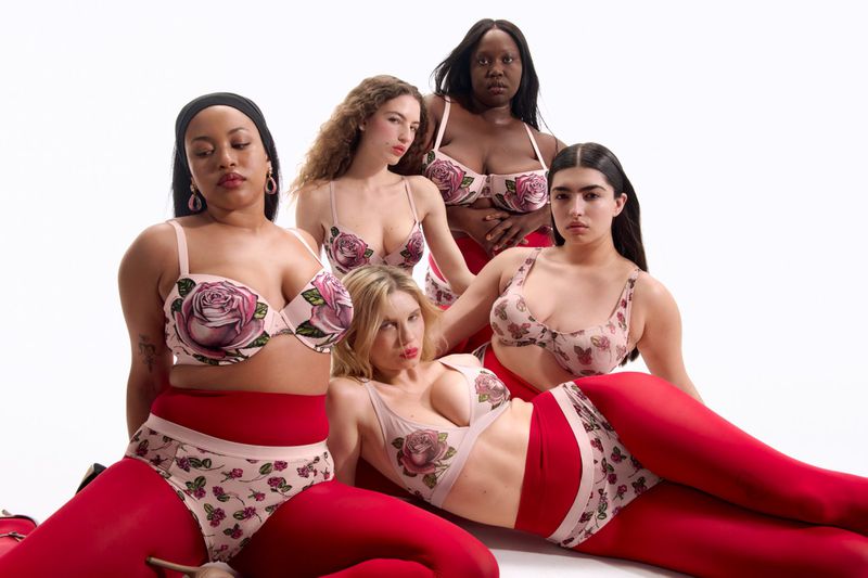 Five diverse women pose in matching floral lingerie and red tights against a white backdrop in a studio setting.