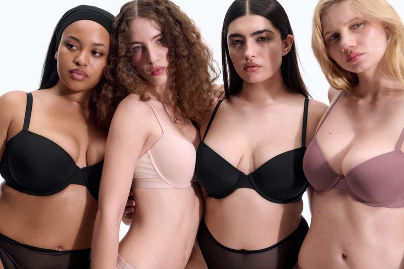 Four diverse female models wearing bras in various shades against a clean white backdrop