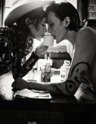 Monochrome image of a man and woman leaning across a diner table, touching foreheads while sharing a small white mug.